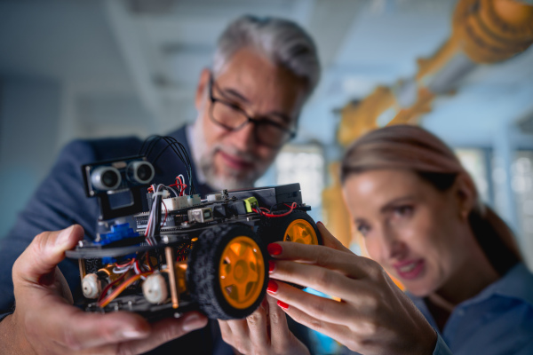 Two robotics engineers assembling robotic car. Concept of modern technology in industries, automated processes, automotive.