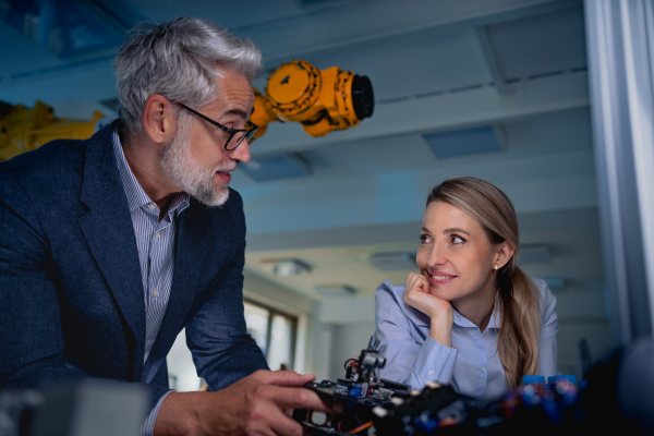 Two robotics engineers working on new project, standing in laboratory. Concept of modern technology in industries, automated processes, automotive.