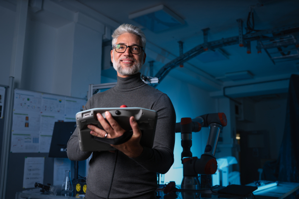 Automation engineer or robotics technician holding remote controller of robotic arm. Concept of modern technology in industries, automated processes and robotics.