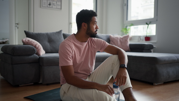 Man with waterbottle after exercising, hydrating himself. A morning workout or meditation routine for a young single man.