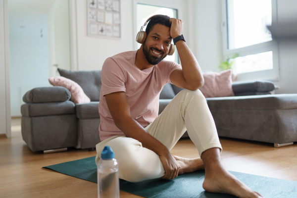 Young man resting after home workout and meditation. Concept of morning or evening workout routine, listening to music through wireless headphones.