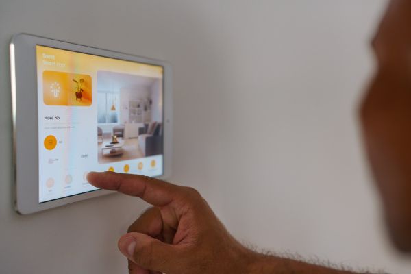 Man adjusting household functions, lighting, security cameras, door locks and thermostat or heating settings in the smart home system screen.