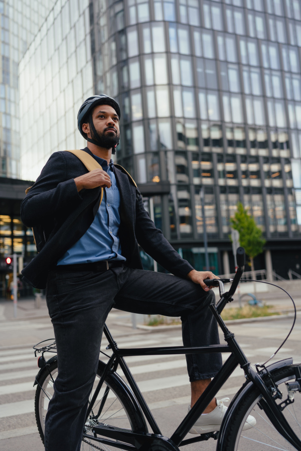 City commuter, businessman traveling from work to home on a bike, wearing backpack and helmet for safety. City lifestyle of single man. Low angle shot.