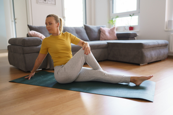 Woman exercising at home, stretching body. Single woman is happy, relaxed, and content with her life. Solo home workout and meditation, morning or evening workout routine.