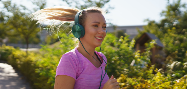 Young woman running outdoors and listening music. Exercising after work for good mental health, physical health, and relieving stress and boost mood. Banner with copy space.