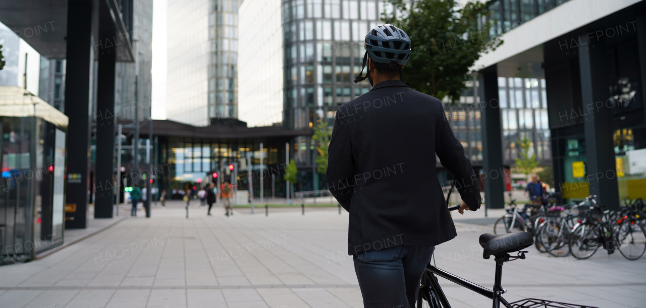 Rear view of city bike commuter leaving work on bicycle after long work day. Banner of city with copy space.