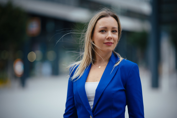 Portrait of beutiful businesswoman standing in front of office building in the city. Blue blazer, business casual outfit for work.