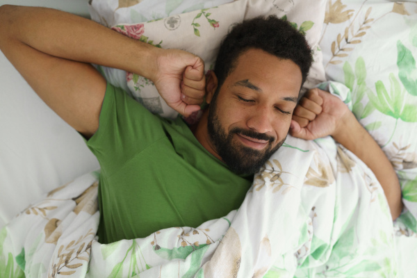 Top view of happy man waking up in bed, stretching arms, smiling in the morning.