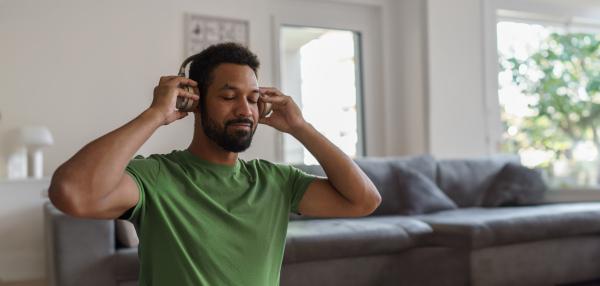 Young man with closed eyes, listening meditating music at home. Morning or evening workout routine, listening to music through wireless headphones. Banner with copyspace.