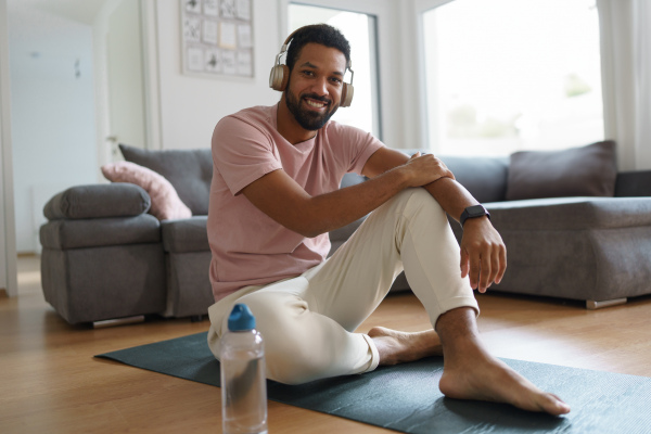 Young man resting after home workout and meditation. Concept of morning or evening workout routine, listening to music through wireless headphones.