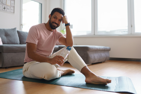 Young man resting after home workout, meditating at home. Concept of morning or evening workout routine, listening to music through wireless headphones.