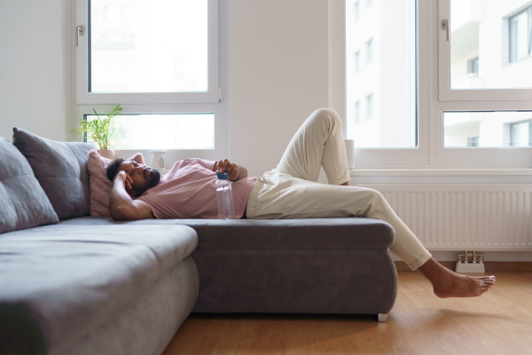 Young man lying on sofa, resting after home workout, meditating at home. Concept of morning or evening workout routine, listening to music through wireless headphones.