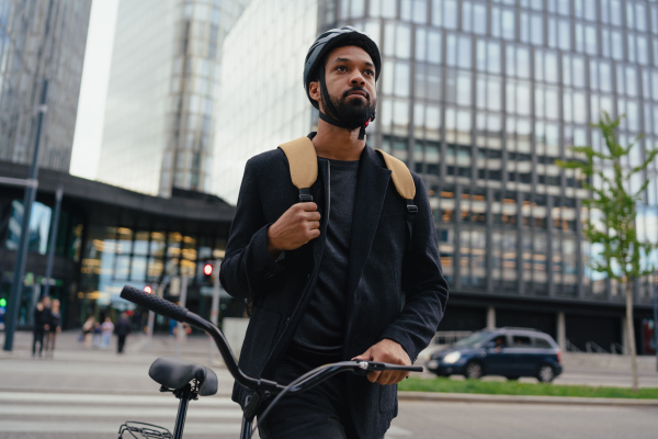 City commuter, businessman traveling from work to home on a bike, wearing backpack and helmet for safety. City lifestyle of single man. Low angle shot.