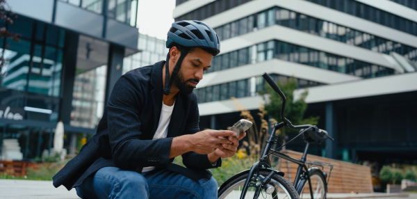 City commuter, sitting on bench, scrolling on smartphone. Businessman traveling from work to home on bike. City lifestyle, banner with copyspace.