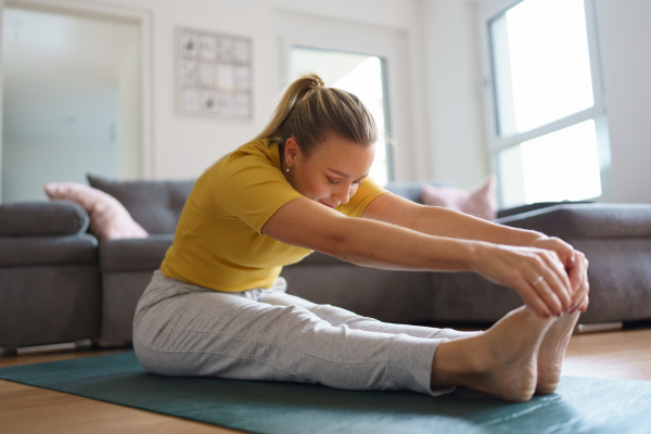 Woman exercising at home, stretching body. Single woman is happy, relaxed, and content with her life. Solo home workout and meditation, morning or evening workout routine.