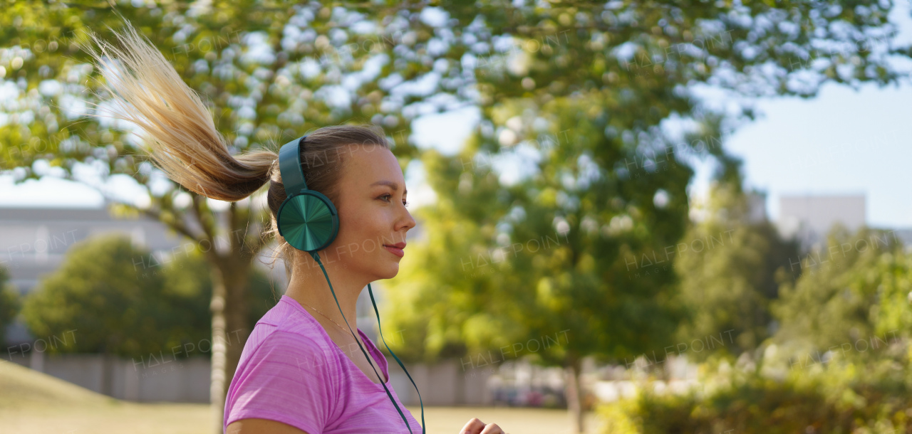 Young woman running outdoors and listening music. Exercising after work for good mental health, physical health, and relieving stress and boost mood. Banner with copy space.