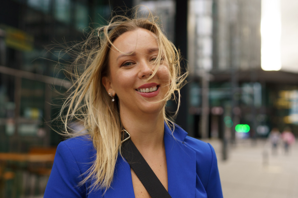 Portrait of beutiful businesswoman standing in front of office building in the city. Blue blazer, business casual outfit for work.