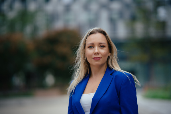 Portrait of beutiful businesswoman standing in front of office building in the city. Blue blazer, business casual outfit for work.