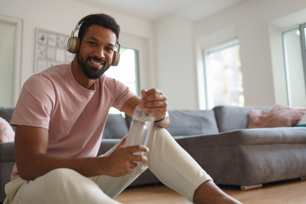 Young man resting after home workout and meditation. Concept of morning or evening workout routine, listening to music through wireless headphones.