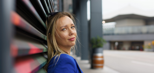 Portrait of beautiful businesswoman standing in front of office building in the city. Blue blazer, business casual outfit for work. Banner with copyspace.