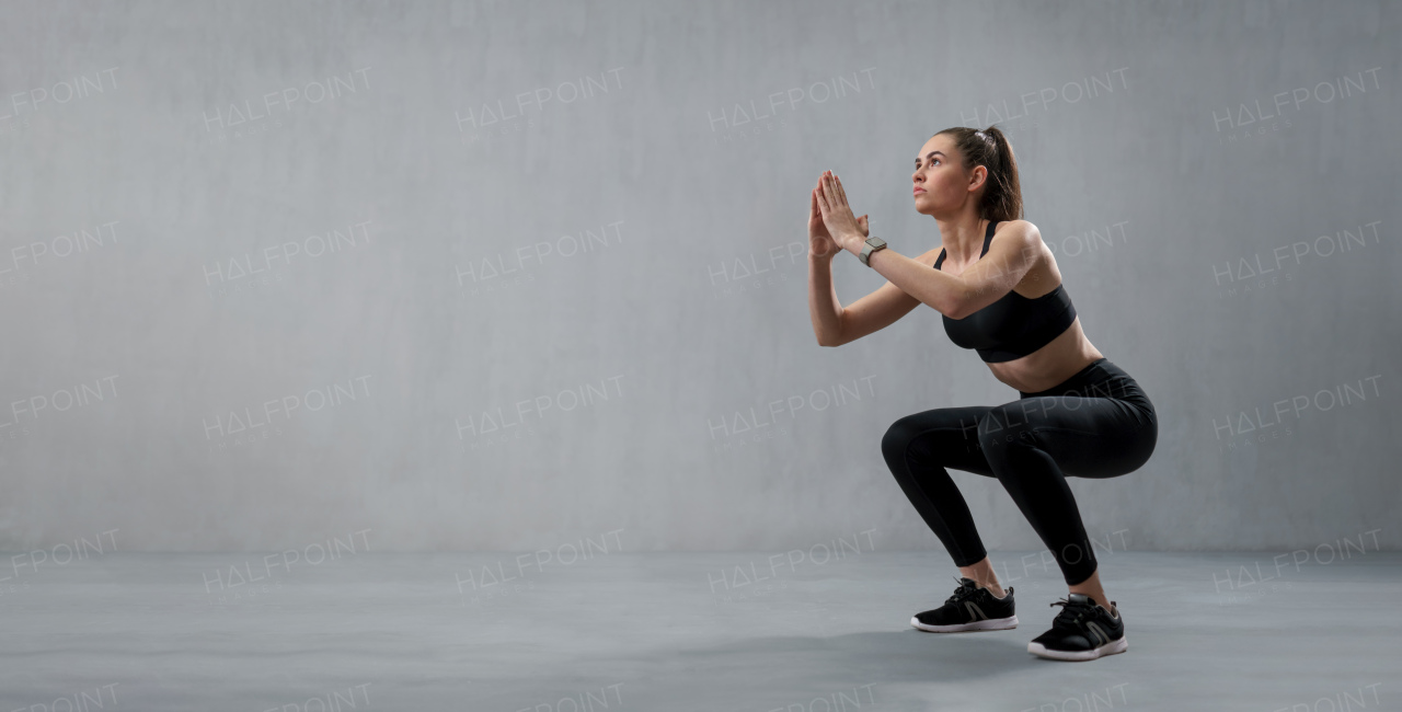 A sports woman in fashion black sport clothes squatting doing sit-ups in gym, over gray background