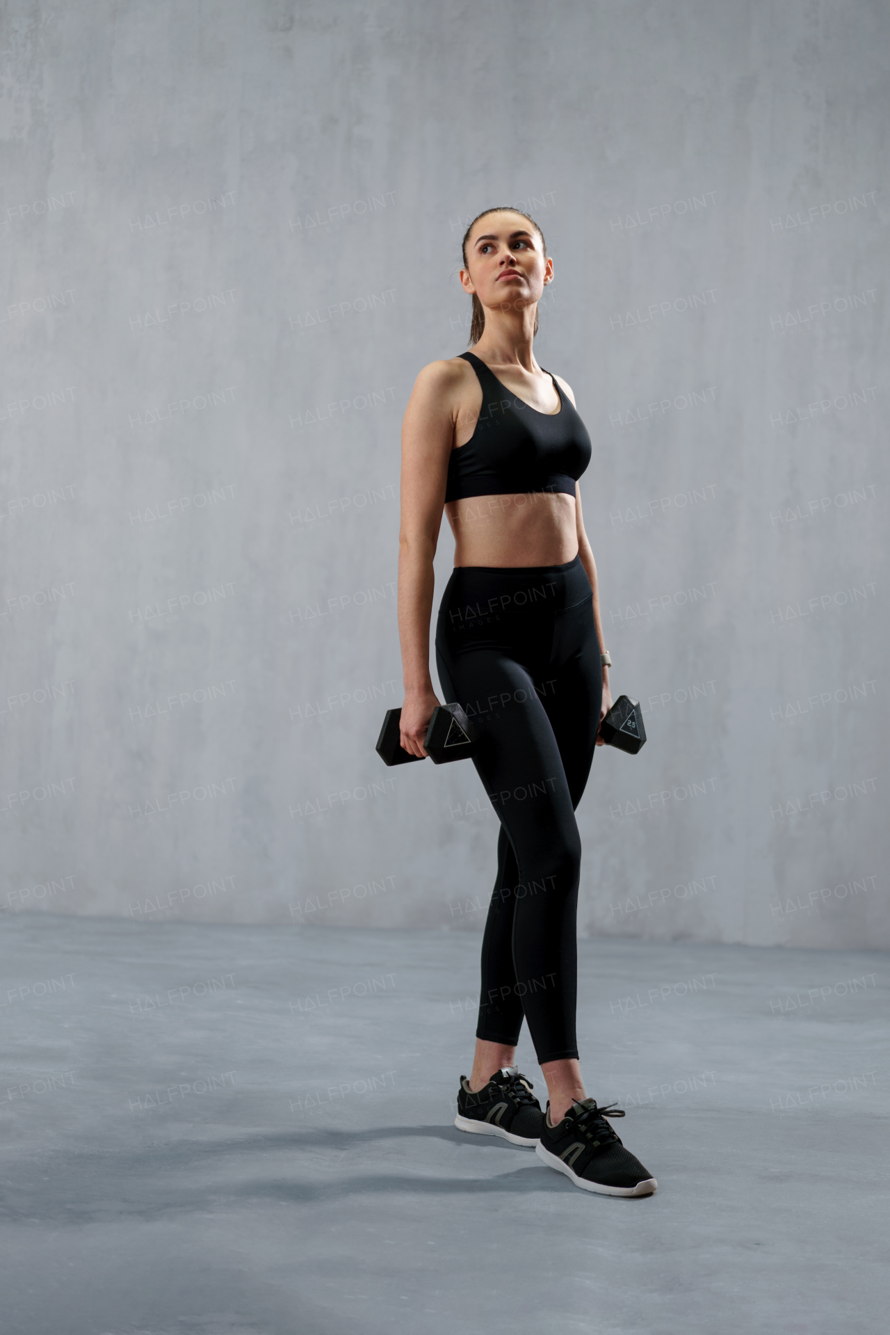 AN athletic fitness woman working out with dumbbells on grey background. Copy space.