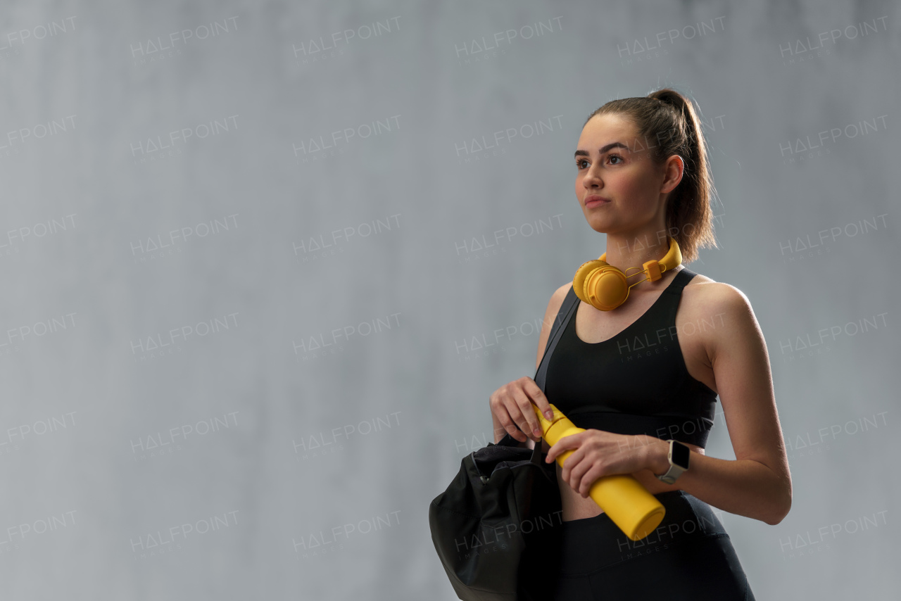 On the way to gym. A young sporty woman in sportswear with fitness bag, wireless headset and bottle over grey background, copy space