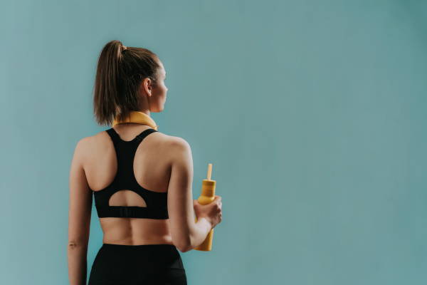 A rear view of young sporty woman in sportswear with wireless headset and bottle over green background, copy space