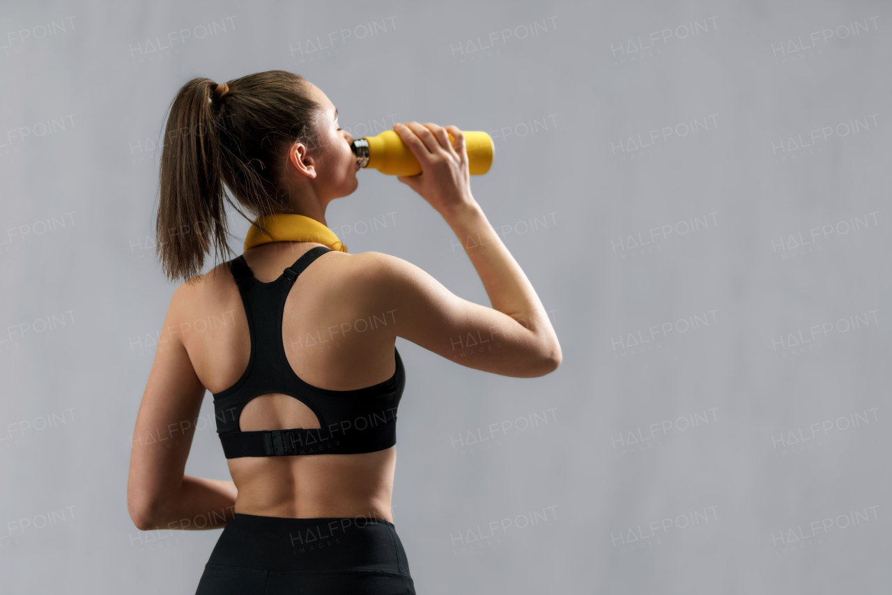 Rear view of a young sporty woman in sportswear with wireless headset drinking from bottle over green background, copy space