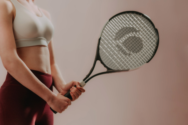 A cut out of young sporty woman in sports clothes holding tennis racket while standing against beige background, copy space