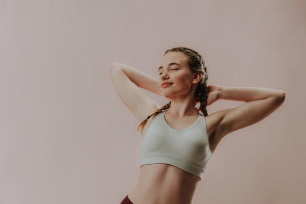 A young sporty woman in sports clothes with eyes closed meditating against beige background, copy space