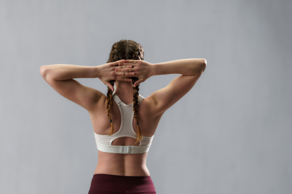 A rear view of young sporty woman in sports clothes stretching arms against grey background, copy space