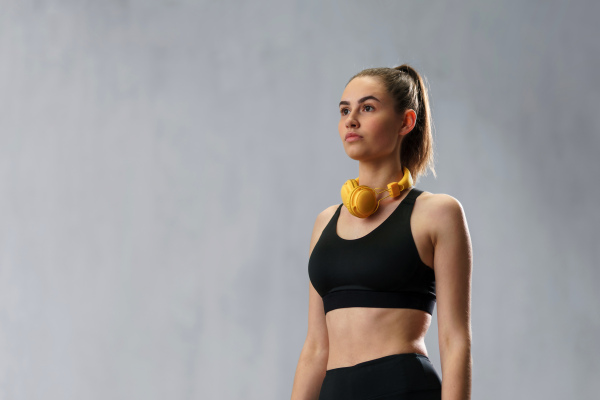 A young sporty woman in sportswear with wireless headset over grey background, copy space