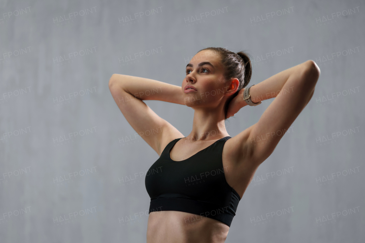 A young sporty woman in sports clotheswith arms behind head against beige background, copy space