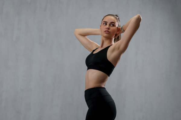 A sports woman in fashion black sport clothes posing in gym, over gray background