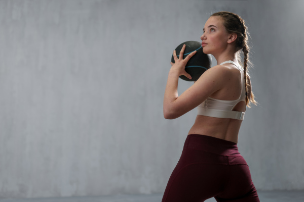 An athletic fitness woman working out with medicine ball on grey background. Copy space.