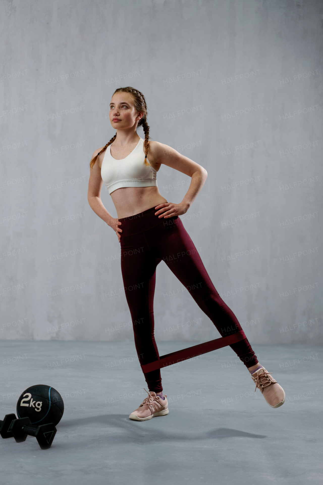 A sports woman in fashion sportswear exercising with elastic band stretch over greay background.