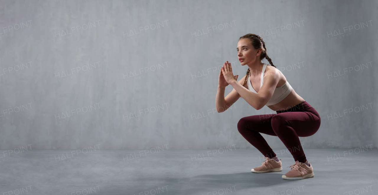 A sports woman in fashion sport clothes squatting doing sit-ups in gym, over gray background