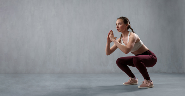 A sports woman in fashion sport clothes squatting doing sit-ups in gym, over gray background