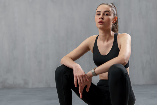 A young sporty woman in sports sitting against grey background, copy space