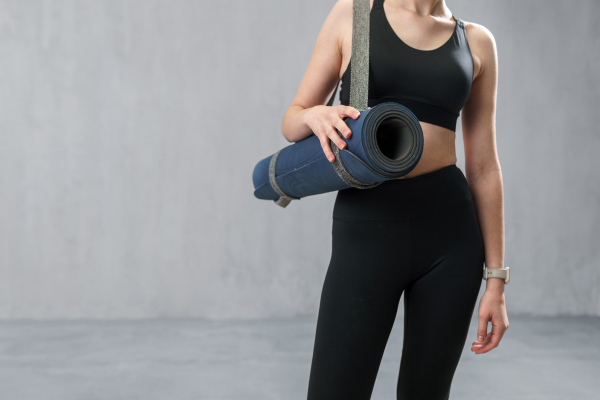 A sports woman in fashion black sport clothes carrying fitness mat in gym, over gray background