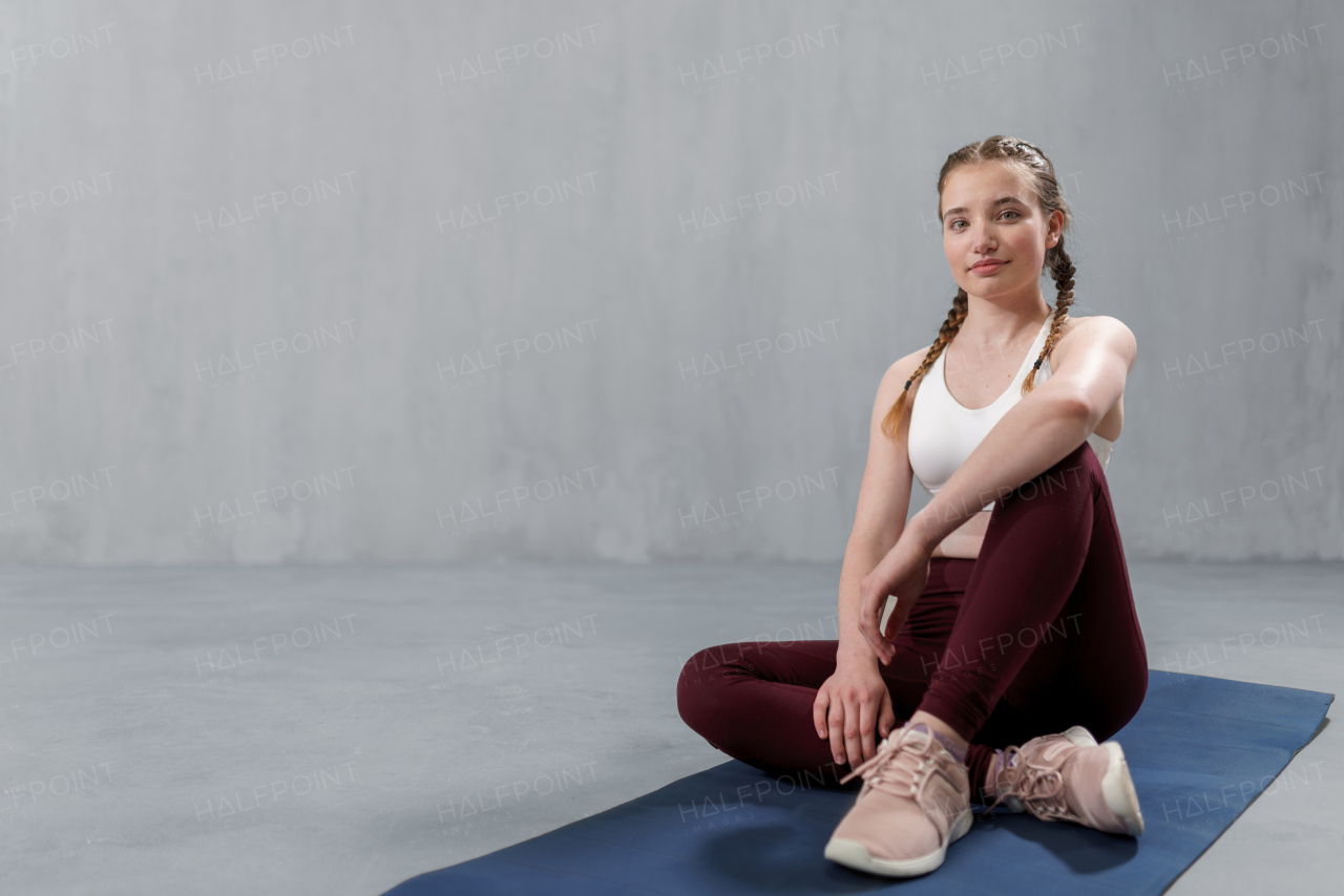 A sports woman in fashion sport clothes working out against grey wall, doing yoga, pilates balancing exercise.