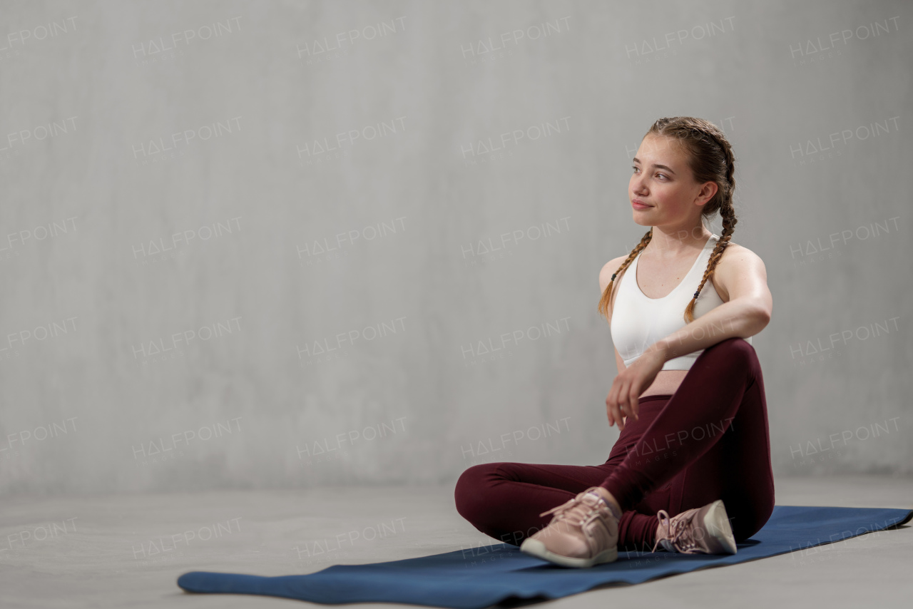 A sports woman in fashion sport clothes working out against grey wall, doing yoga, pilates balancing exercise.