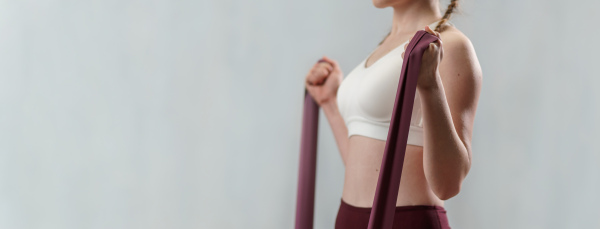 A close-up of sports woman in fashion sportswear exercising with elastic band stretch over greay background.