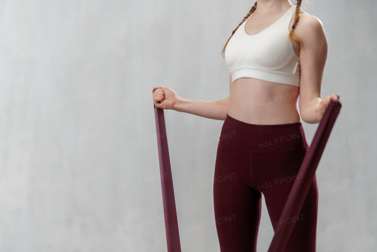 A close-up of sports woman in fashion sportswear exercising with elastic band stretch over greay background.