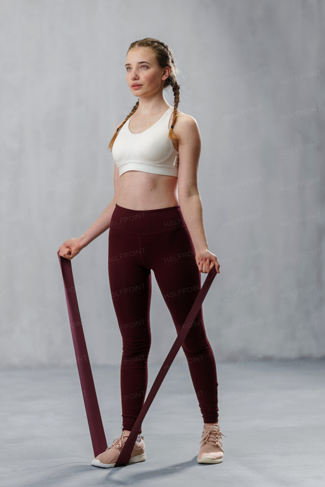 A sports woman in fashion sportswear exercising with elastic band stretch over greay background.