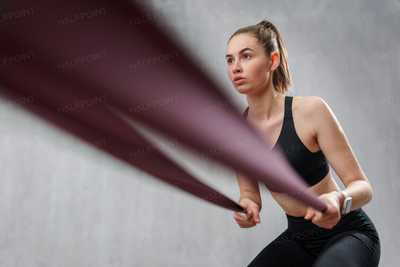 A sports woman in fashion sportswear exercising with elastic band stretch over greay background.