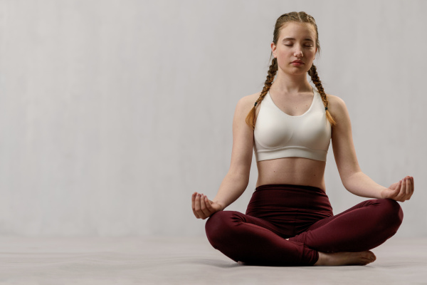 A young healthy woman in black sportsclothes practising yoga in studio, in a yoga position, copy space