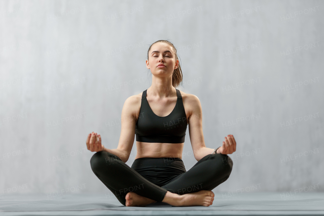 A young healthy woman in black sportsclothes practising yoga in studio, in a yoga position, copy space