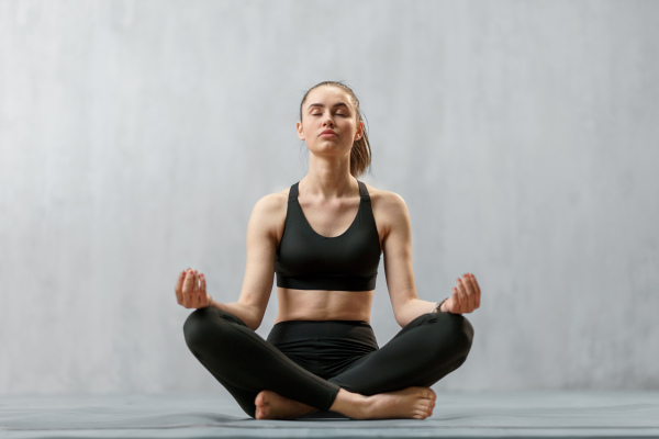 A young healthy woman in black sportsclothes practising yoga in studio, in a yoga position, copy space